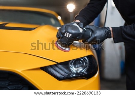 Car detailing and polishing concept. Hands of professional car service male worker, with orbital polisher, polishing yellow luxury car hood in auto repair shop. Royalty-Free Stock Photo #2220690133