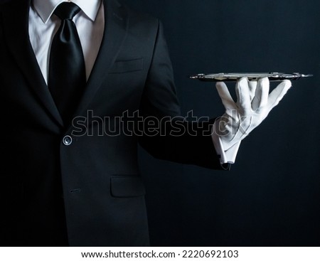 Portrait of Butler or Waiter in Black Suit and White Gloves Holding Serving Tray. Concept of Service Industry and Elegant Hospitality. Royalty-Free Stock Photo #2220692103