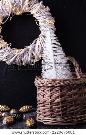 Composition with simple black and white New Year decorations. White trees in basket  against black textured background. Scandinavian minimalistic style. Still life.