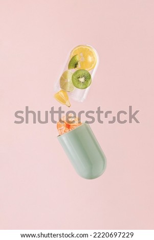 Green transparent pill with lemon, tangerine, kiwi and lime on isolated pastel coral pink background. Minimal pharmaceutical abstract concept of supplements. Natural fruit sources of vitamin C. Royalty-Free Stock Photo #2220697229