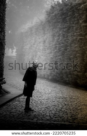 A woman stands in a square with a mystical atmosphere and looks up. Black and white photo.