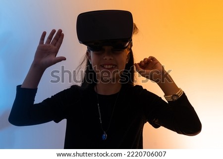 A teenage girl with hair wearing virtual reality glasses watches movies or plays video games shows a sign of gratitude with her hands. Funny girl looking in VR glasses holding hands together.
