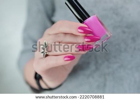 Female hand with long nails and a bottle bright neon pink fuchsia color nail polish