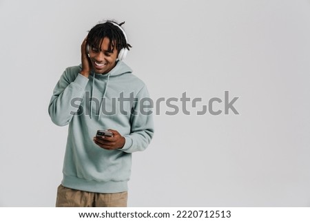 Young african man listening music with headphones using mobile phone isolated over white background Royalty-Free Stock Photo #2220712513
