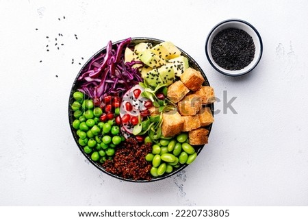 Healthy vegan diet food. Buddha bowl with quinoa, fried tofu, avocado, edamame beans, peas, radish, red cabbage and sesame seeds. White kitchen table background, top view 