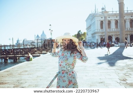 smiling modern woman in floral dress with hat exploring attractions on embankment in Venice, Italy.