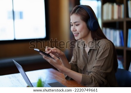 Portrait of a smiling Asian teenage girl wearing headphones and using a computer for online video conferencing in a library.