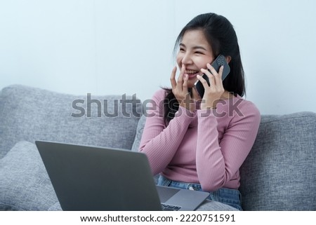 Portrait of a beautiful Asian teenage girl using her phone and computer sitting on the sofa at home.