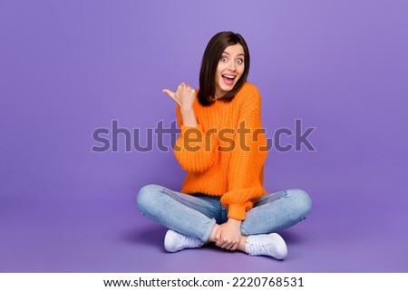 Full size photo of lovely young woman sit floor point copyspace dressed stylish orange knitted look isolated on purple color background Royalty-Free Stock Photo #2220768531
