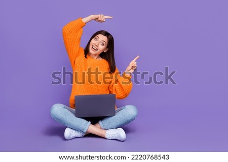 Full size photo of cute young woman work netbook point copyspace dressed stylish orange knitted outfit isolated on purple color background