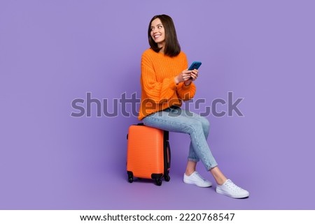 Full size photo of cute young woman hold device wait taxi service wear trendy orange knitwear garment isolated on violet color background