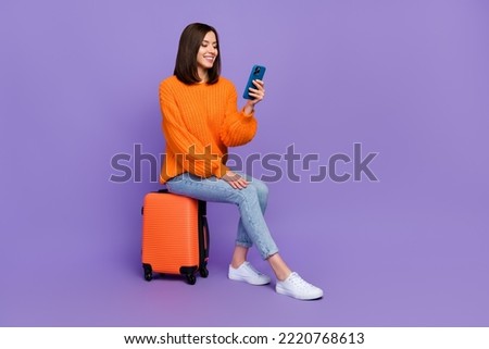 Full size photo of lovely young girl hold device read news wait departure dressed orange knitted outfit isolated on purple color background