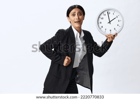 Business woman holding a wall clock in a black business suit and glasses showing signals gestures and emotions on a white background, freelancer job online time management