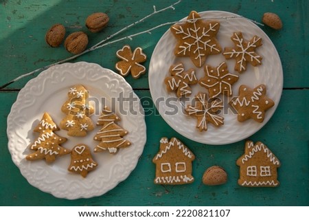 Painted traditional Christmas gingerbreads arranged on white plates on old vintage painted table in daylight, various xmas shapes trees, houses and snowflakes