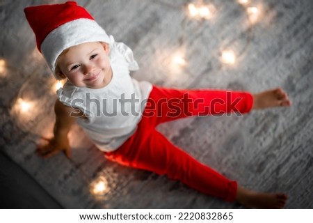 A cute little girl in a red hat and white shirt. Christmas concept with little kid and garland on background in blur. High quality photo