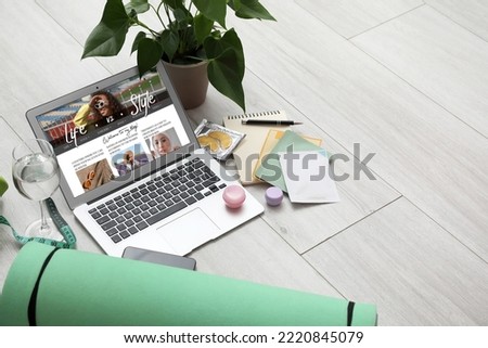 Laptop with open page of lifestyle blog, mobile phone, skincare products, houseplant and fitness mat on light wooden background