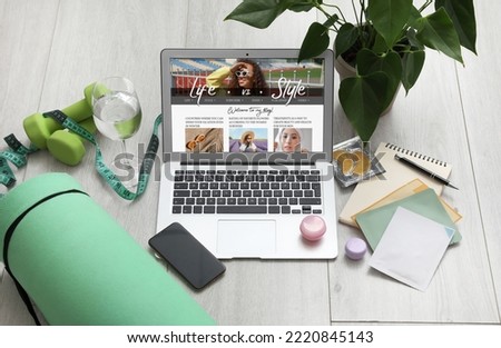 Laptop with open page of lifestyle blog, mobile phone, skincare products, houseplant and dumbbells on light wooden background