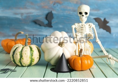 Halloween pumpkins with skeleton, spiders and witch's hat on color wooden background