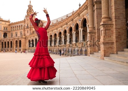 Beautiful teenage woman dancing flamenco in a square in Seville, Spain. She wears a red dress with ruffles and dances flamenco with a lot of art. Flamenco cultural heritage of humanity. Royalty-Free Stock Photo #2220869045