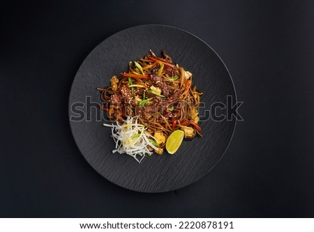 Stir fry soba noodles with vegetables and beef in black plate. Noodles on a dark background. Traditional Asian fast food, wok menu. Flat lay, top view from above. Chinese, Japanese or Thai cuisine Royalty-Free Stock Photo #2220878191