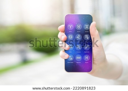 female hand shows a mobile phone with an astrological application with zodiac signs