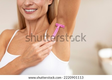 Smiling caucasian mature woman shaving her armpit hair with razor, making morning routine at home, cropped, close up, copy space. Depilation, beauty and skin care, hygiene
