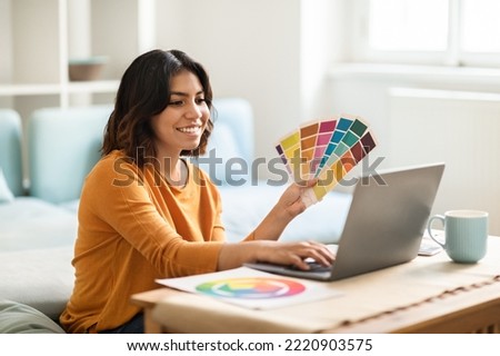 Arab Female Freelance Graphic Designer Working With Laptop And Color Swatches At Desk In Home Office, Smiling Middle Eastern Woman Choosing Colour Gamma For New Design Project, Free Space