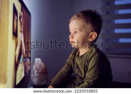 Child entertainment and family values. The baby boy is right in front of the TV and stares at the cartoon. Entertaining a child before bed at night The toddler does not blink as he looks at the screen