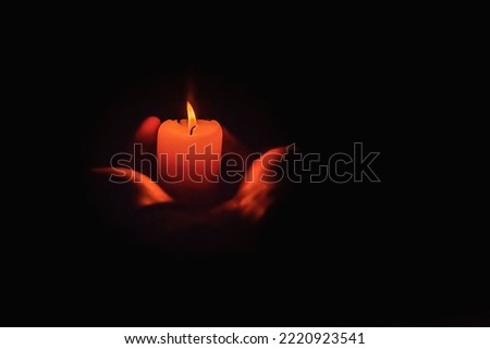 Human hands holding a burning candle in the dark. Adult woman with a red candle on the black background.Selective focus.Closeup.Copy space.
