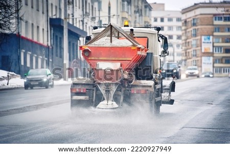 Snow plow truck removing snow and spreading salt and grit on snowy city road during blizzard. Road and highway maintenance gritter truck spread de-icing salt in winter. Truck sprinkled salt on road