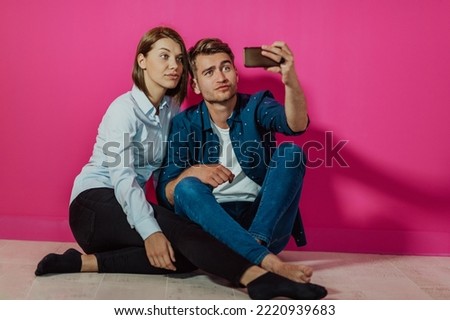 A happy young couple sitting on the floor in the house and making selfie