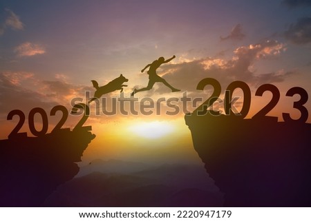 Silhouette dog and young man jumping from 2022 to 2023 at cliff on sunset. New year and success concept. Royalty-Free Stock Photo #2220947179