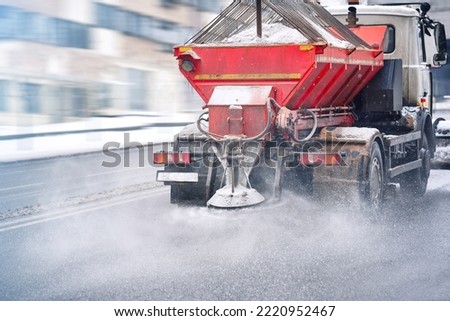 Road and highway maintenance gritter truck spreading de-icing salt on road in winter. Salt spreading. Snow plow service truck removing snow and spreading salt on snowy city road during blizzard Royalty-Free Stock Photo #2220952467
