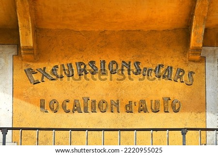 vintage advertising sign in french language (translated as Car tours and car rental) on rustic wall