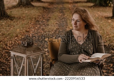 Close portrait picture of a woman sitting on a yellow armchair with a book in her hands. She is holding the book while looking to the right side dreaming. 