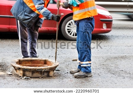 Road workers repair old sewer manholes on the carriageway against the background of passing cars.