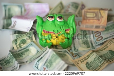 Sculpture piggy bank in the form of a green frog surrounded by money.Ceramic piggy bank on the table. Dollar bills lie near the piggy bank in the form of a frog.
