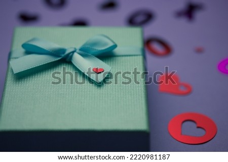 Blue gift box with bow and little red heart. Pink hearts on purple background. Gift given with love to boyfriend, girlfriend, husband, wife, sweetheart lovers at Valentine's Day at February 14.  Royalty-Free Stock Photo #2220981187