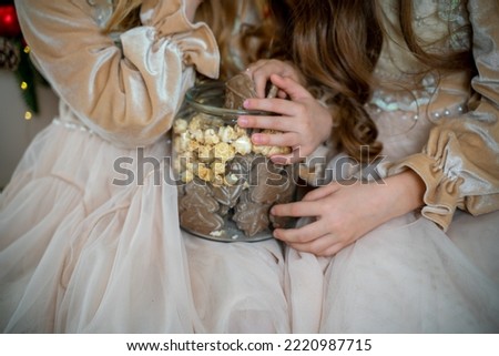 Two cute little girls in beige dresses are sitting on the table holding cookies. New Year decoration. Luxurious New Year's interior.