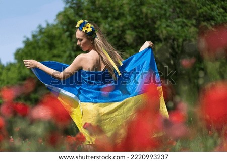 A young blonde Ukrainian woman stands in a field of Red Poppy flowers holding the flag of Ukraine showing her support for the war in her native country of Ukraine