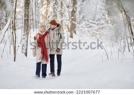Full length portrait of happy senior couple enjoying walk in winter forest and looking at each other, copy space