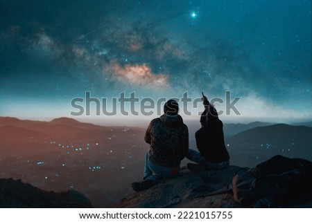 silhouette of a couple sitting on top of a hill looking at the stars over the city Royalty-Free Stock Photo #2221015755