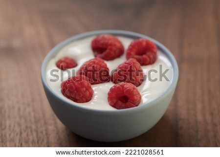 Yogurt with fresh raspberries in blue ceramic bowl on walnut table
