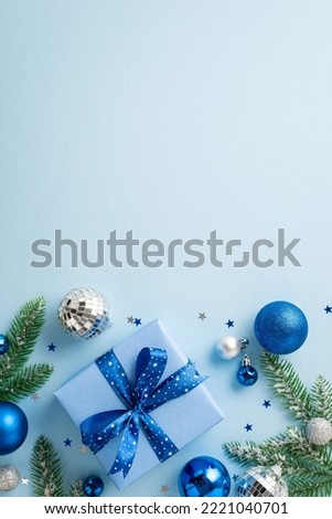 New Year concept. Top view vertical photo of blue and white baubles disco ball stylish giftbox with ribbon bow fir branches and confetti on isolated pastel blue background with copyspace