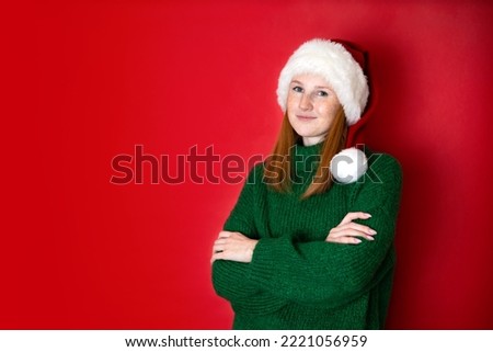 Merry Christmas Portrait of a beautiful young teenage girl in a cozy knitted green sweater and Santa's hat. The red background is the place for the text. High quality photo