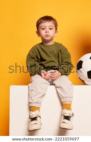Charming cute little toddler boy sitting on big box and looking at camera. Emotions, kids fashion, happy childhood concept. Looks calm and sad. Copy space for ad