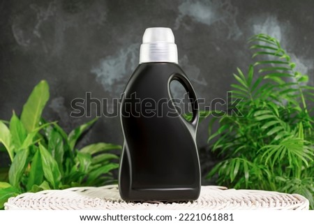Natural laundry detergent mockup for washing black clothes. Washing detergent concept with bottle of washing gel or fabric softener on laundry basket on black background with house plants. Laundry day