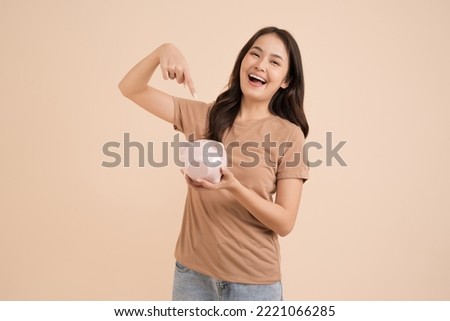 Happy young woman holding piggy bank standing in the studio brown background