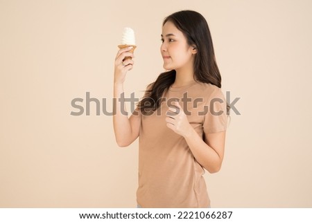 Happy young woman eating ice cream standing on brown background