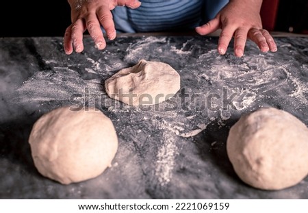 An overhead photo of kid's hands, some sprinkled flour and wheat dough on the marble table. Child's hands making the dough for pizza. Little child cooking dough or pastry